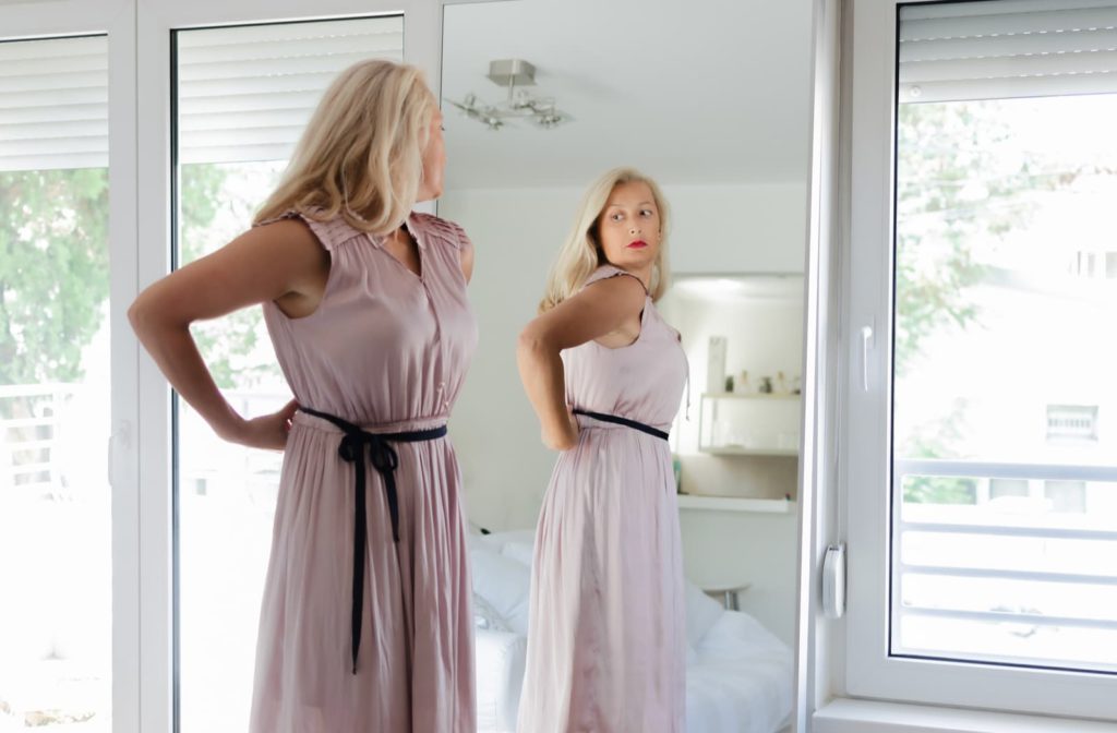 Woman looking into a full-length mirror disappointed in her stubborn fat areas