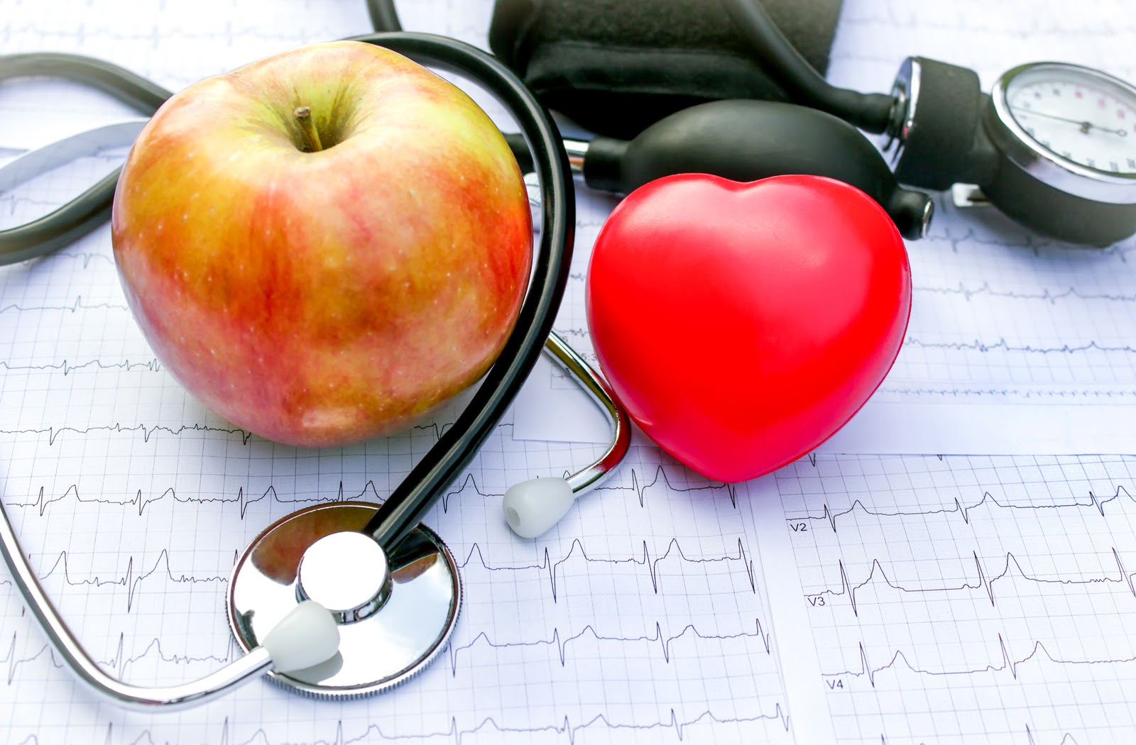 An apple, bright red heart, and a stethoscope laid on top of an Electrocardiogram chart to illustrate good health.