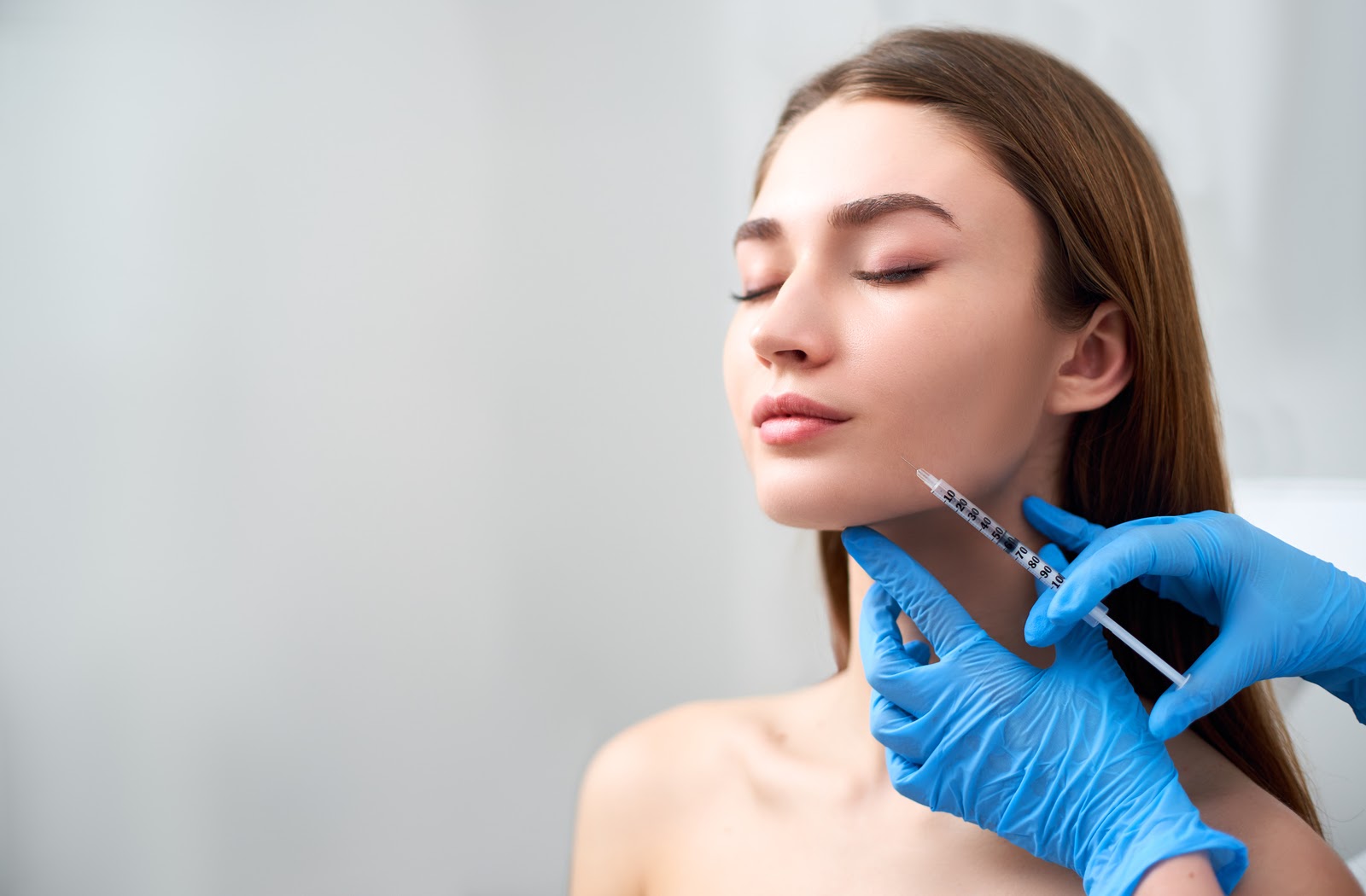 Young woman receiving dermal filler by professional wearing gloves.