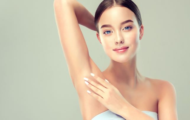 Young woman holding her arms up and showing underarms after laser hair removal