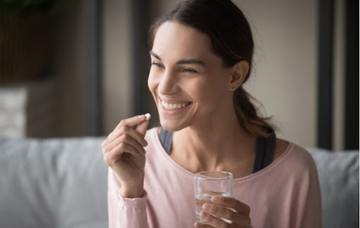 A smiling woman takes a supplement with water.