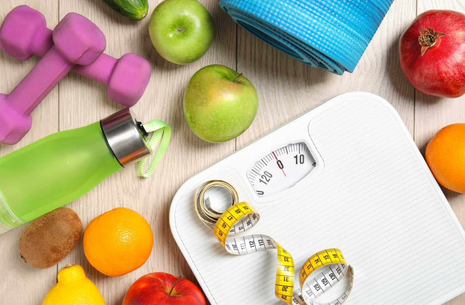 White scale surrounded by different fruits and weight loss equipment.