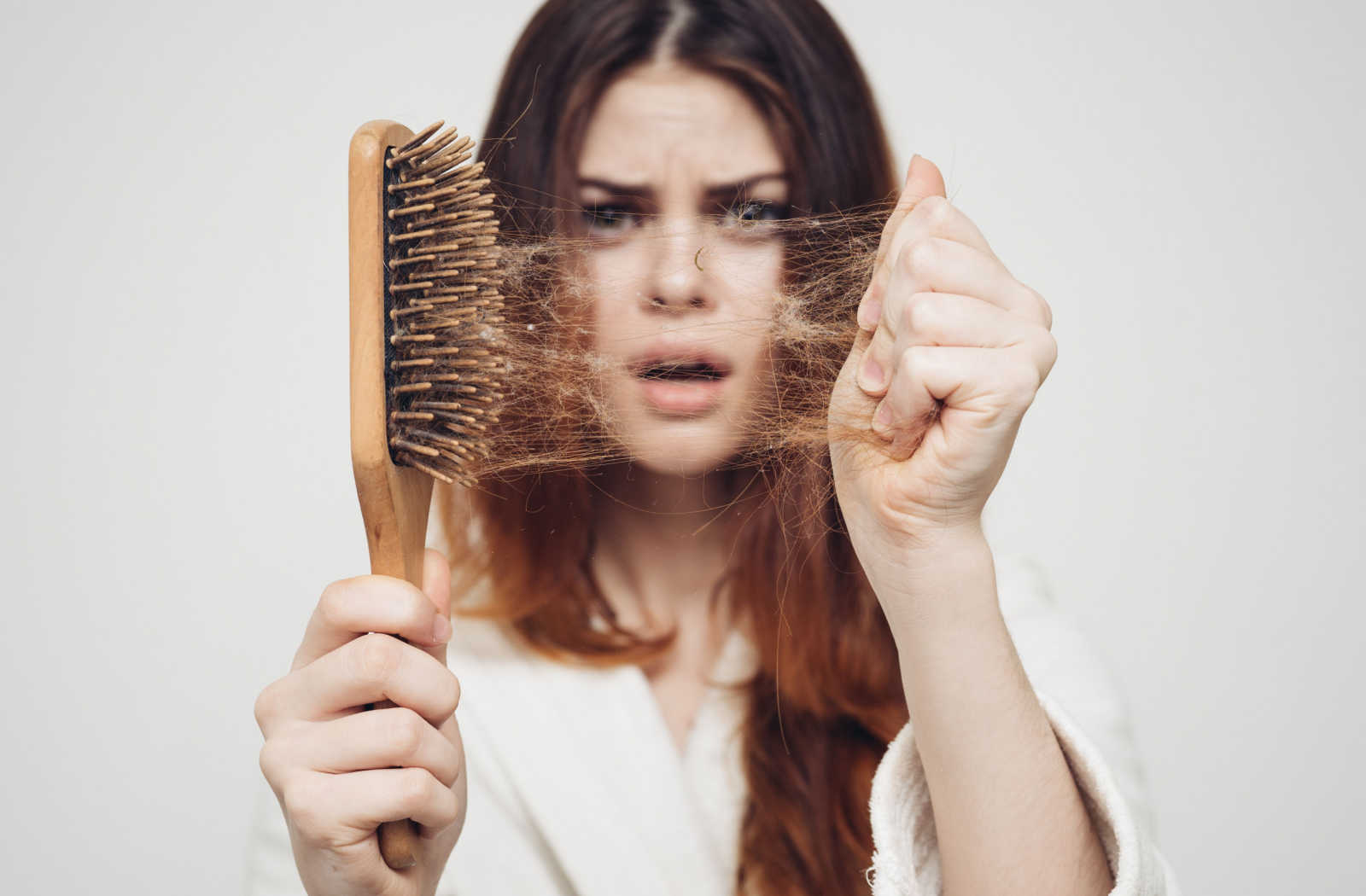 A woman holding a hairbrush with a clump of hair pulled from it.