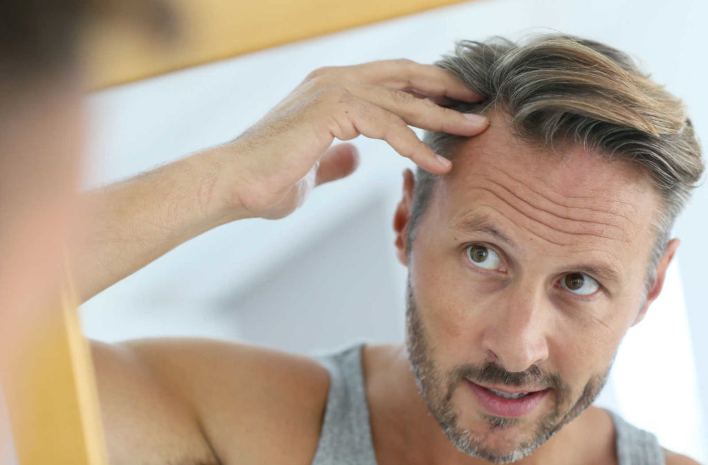 A man examining his hair loss in a mirror.