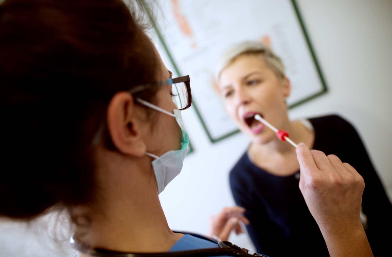 Rear view of a female medical professional holding buccal cotton swab and test tube ready to collect DNA from a woman.