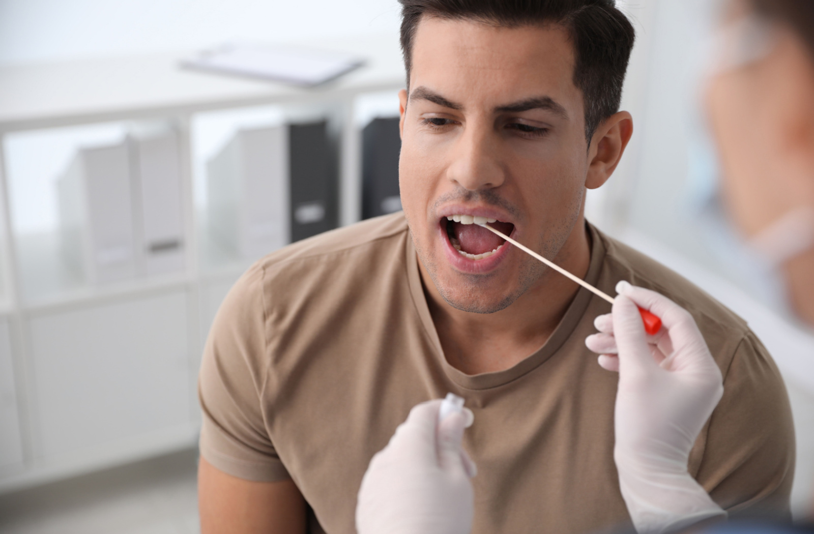 A female medical professional taking a saliva sample for DNA test from man in a clinic.