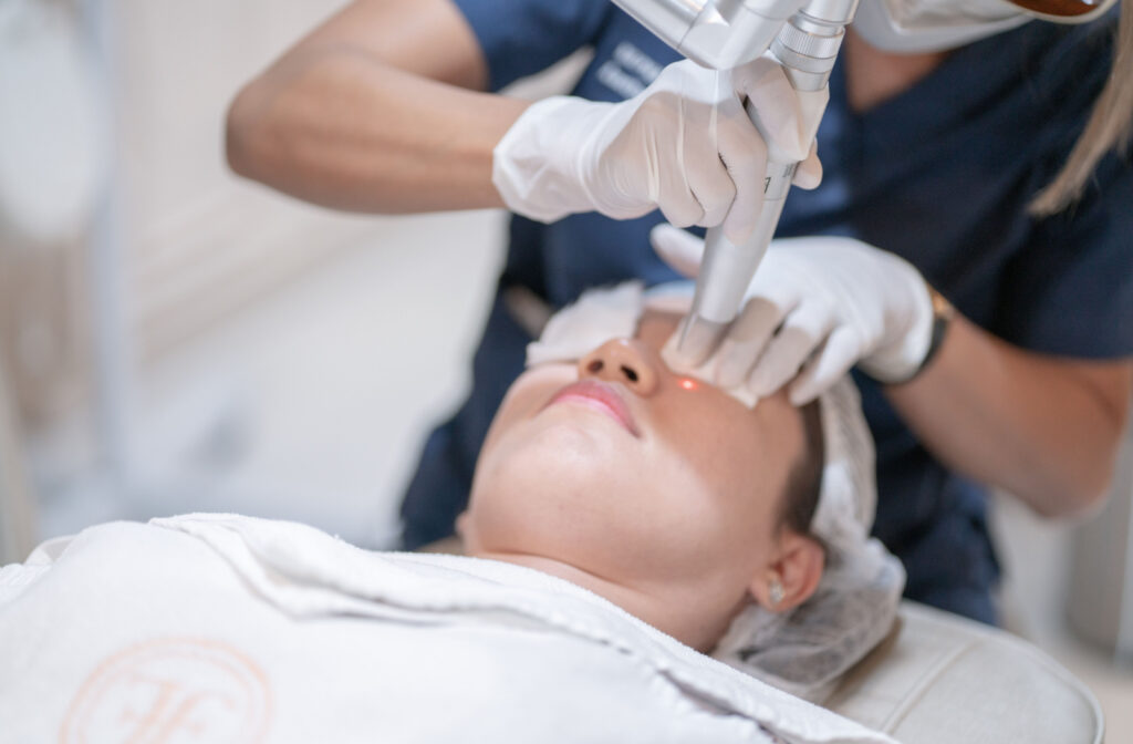 An aesthetician performing a laser treatment on a woman using specialized equipment.