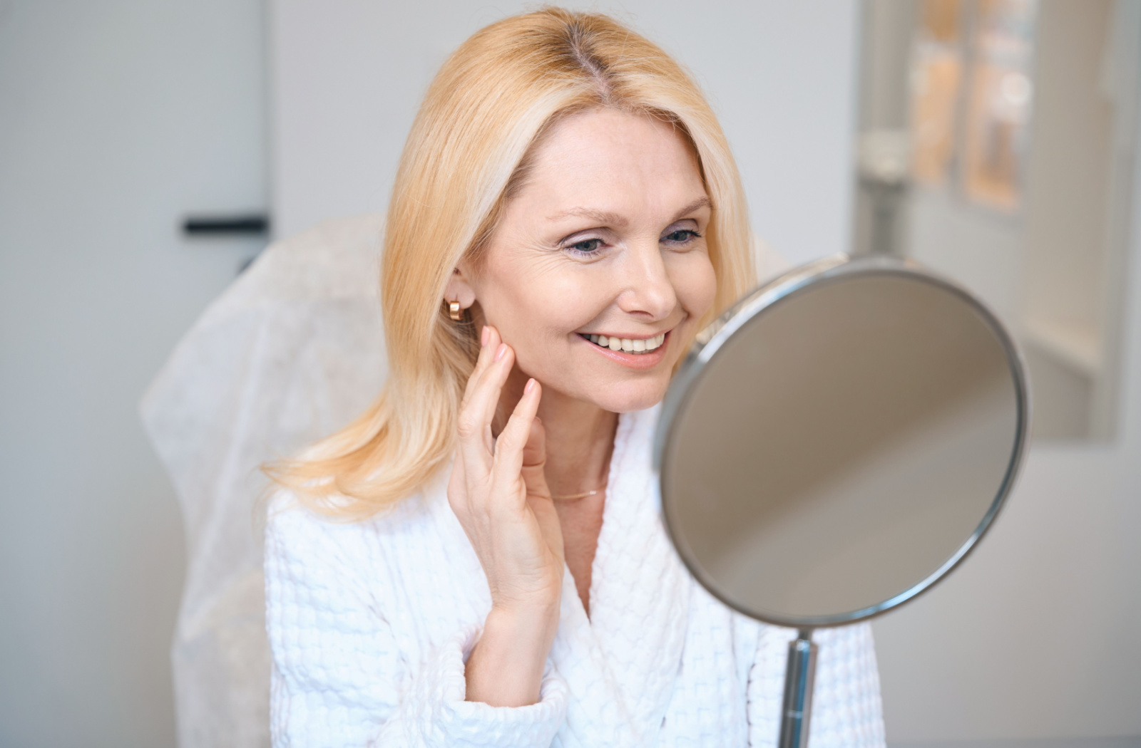 Smiling woman looking at her reflection in a mirror at an aesthetician clinic.