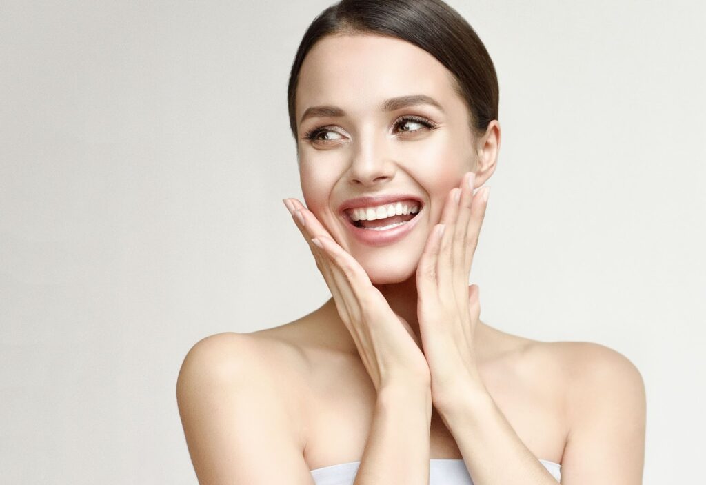 A young woman smiling with her hands around her face showing off her microneedling results.