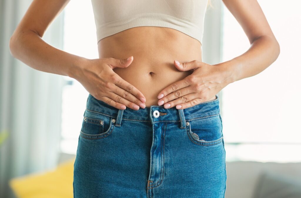 A person with their hands on their naked stomach wearing jeans highlighting a sculpted body.