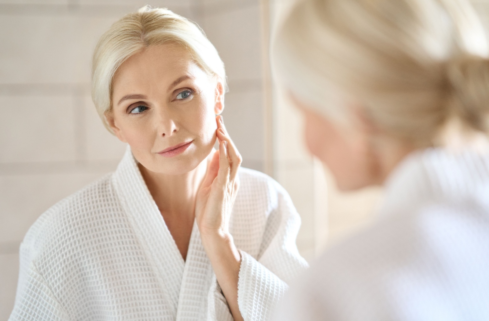 Someone examines their face in their bathroom mirror after skin tightening treatments.