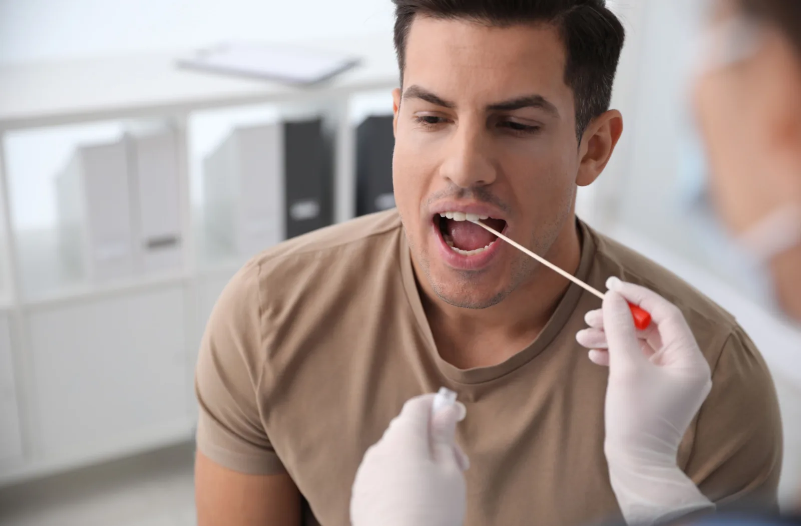 A female medical professional taking a saliva sample for DNA test from man in a clinic.